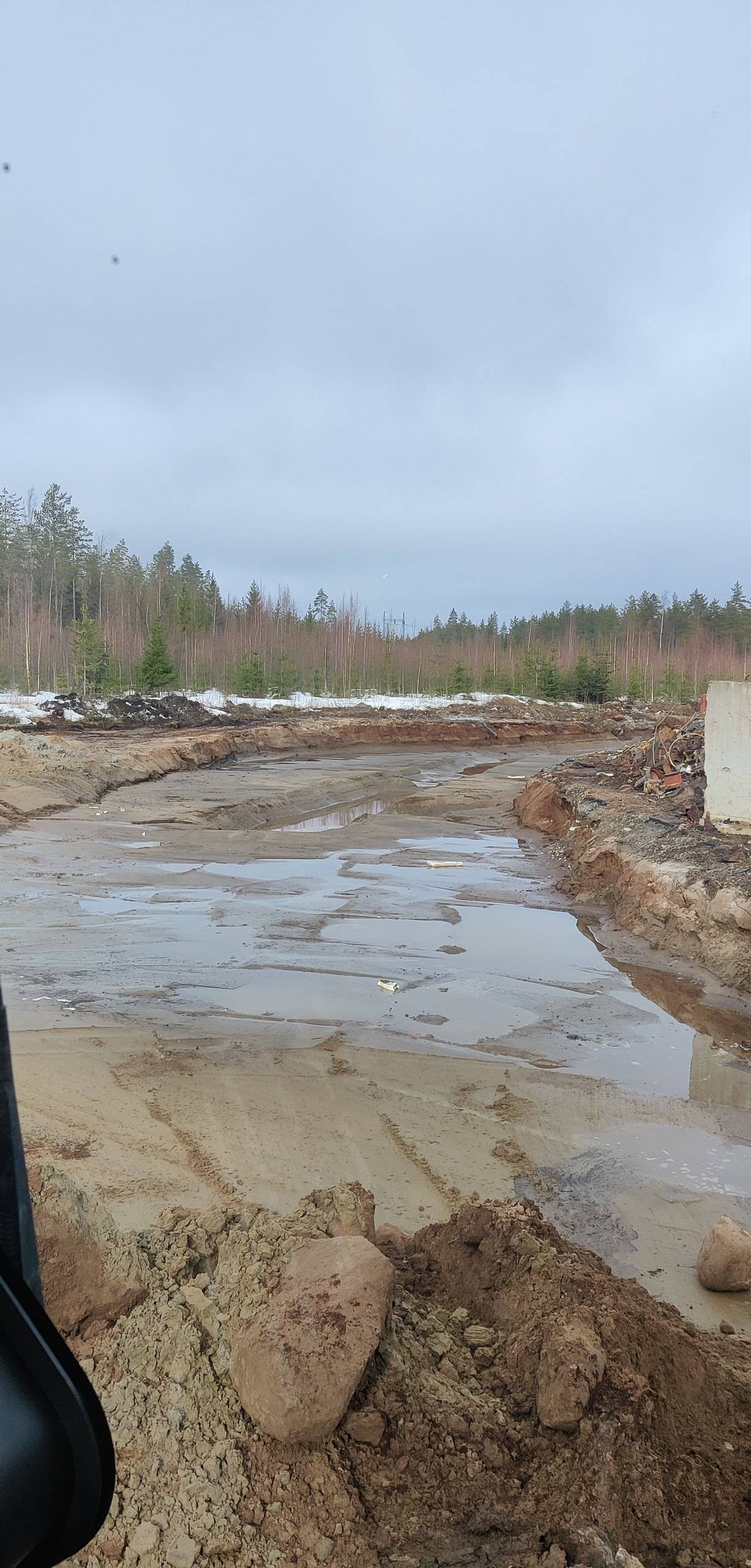 Kaivettu ja tasattu tonttialue keväällä, pinnalla sulamisvettä ja etualalla kiviä